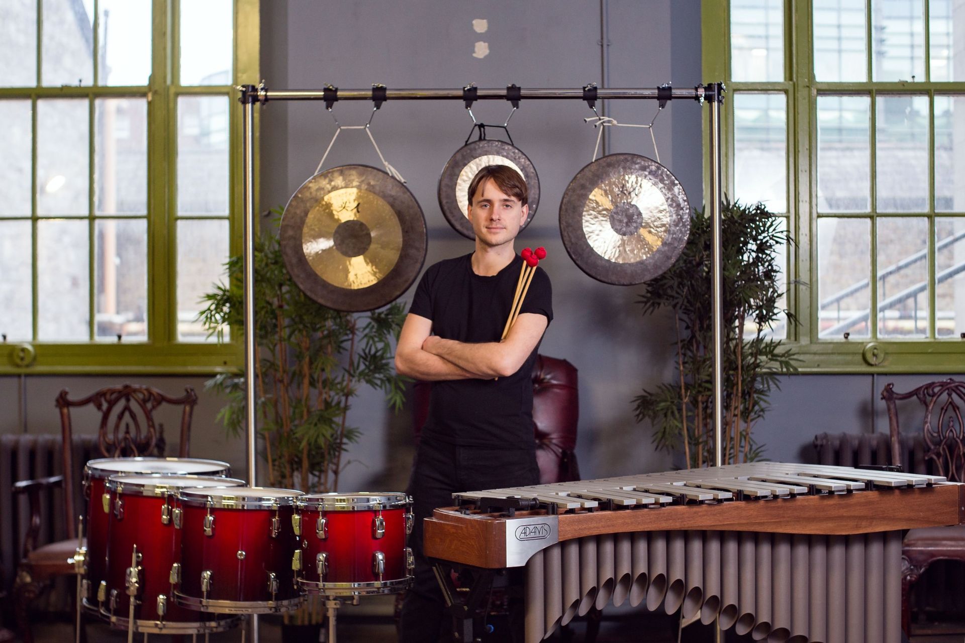 Alex Petcu standing among hanging gongs, with drums and a vibraphone